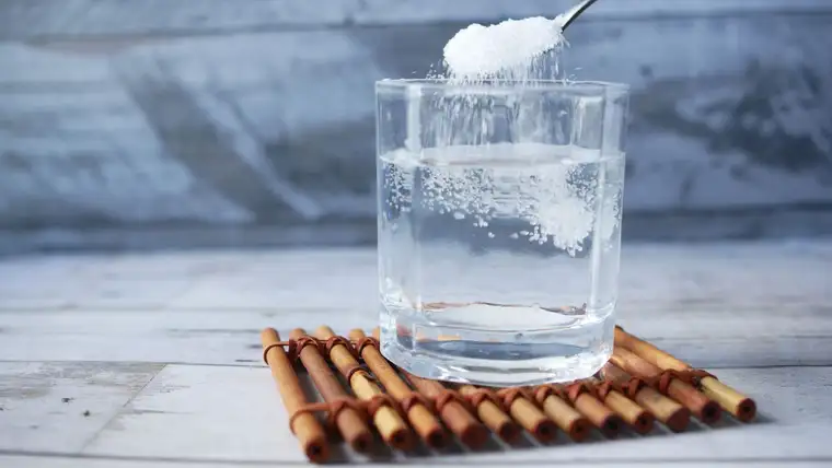 Spoonful of white soda crystals being stirred into a glass of water