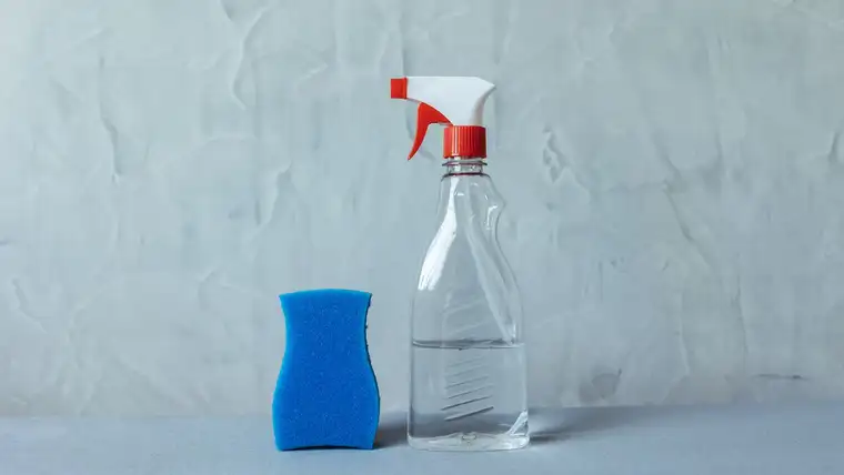 Clear spray bottle of diluted white vinegar beside a blue sponge