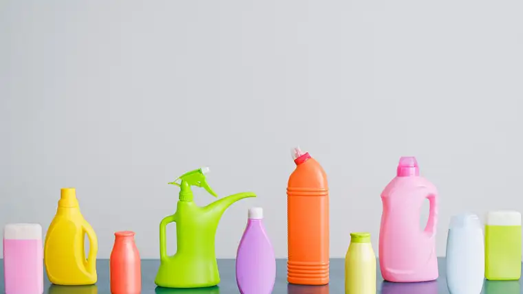 Row of colorful unlabeled cleaning product bottles and a spray bottle on a counter