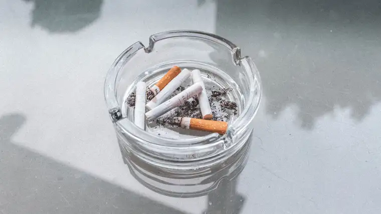 Glass ashtray full of cigarette butts and ash on a gray table