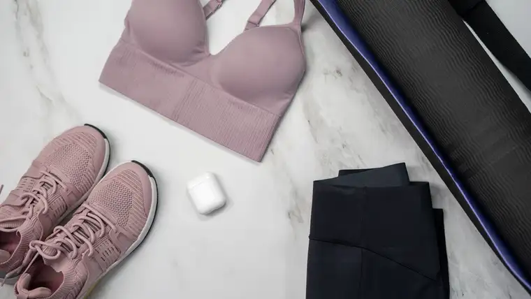 Workout clothes, sneakers and a rolled yoga mat laid out on white marble