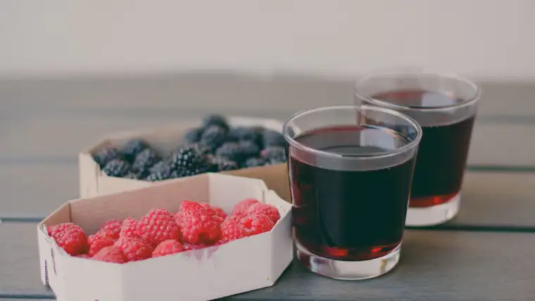Boxes of fresh blueberries and raspberries beside glasses of dark berry juice