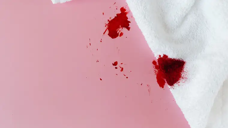 Bright red blood stain soaking into a white terry towel on a pink surface