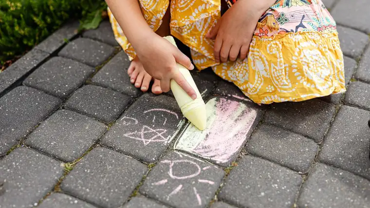 Child in a yellow skirt drawing with thick chalk on paving stones