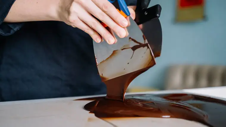 Melted dark chocolate poured and spreading across a white kitchen counter
