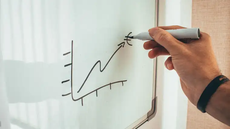 Hand drawing a rising line graph on a whiteboard with a dry erase marker
