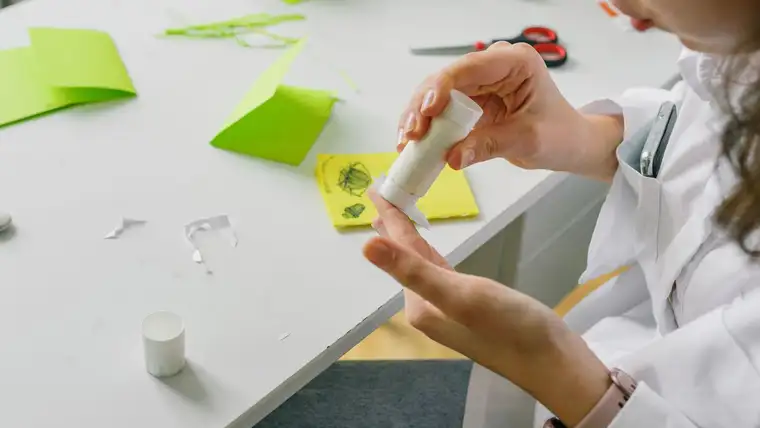 Hands using a glue stick on paper craft projects at a white table