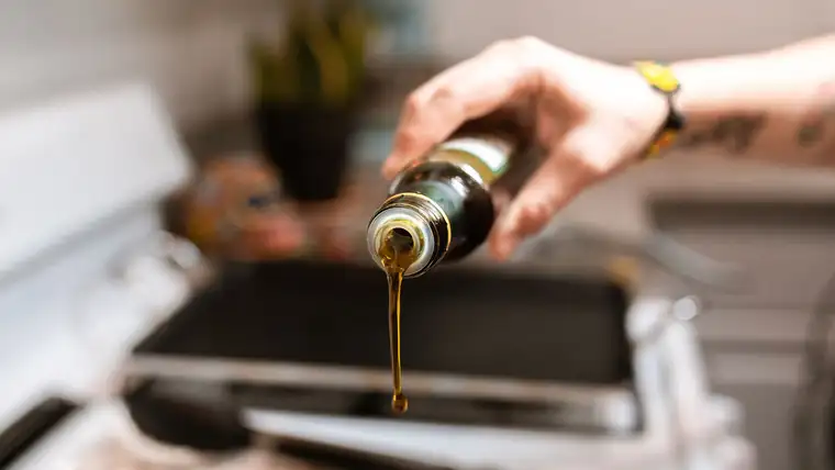 Cooking oil pouring from a bottle toward a pan on a white stove
