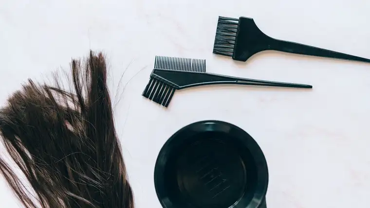 Hair dye brushes, black mixing bowl and a strand of dark hair on white