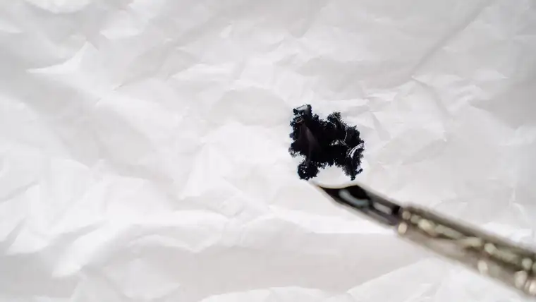 Black ink blot on crumpled white paper beside a dipped brush tip