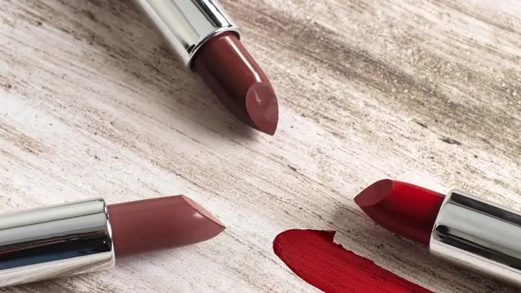 Three lipsticks beside a bold smear of red lipstick on pale wood