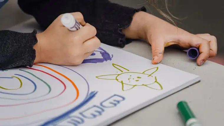Child drawing with washable markers, with marker ink smudged on her fingers