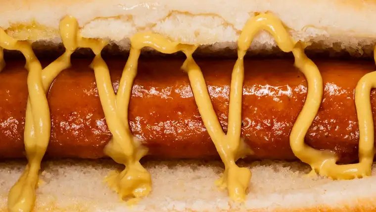 Close-up of yellow mustard zigzagged over a hot dog in a soft bun