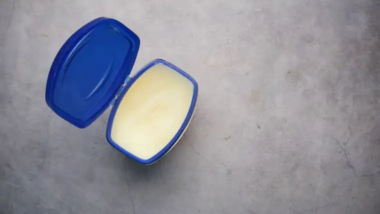 Open tub of petroleum jelly with a blue lid on a gray surface
