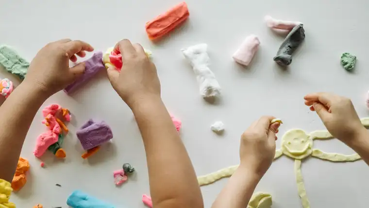 Children's hands shaping colorful modeling dough pieces on a white table