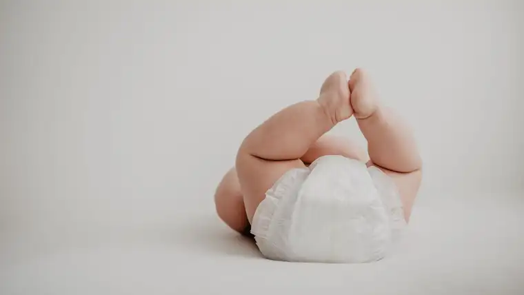 Baby legs raised in a white disposable diaper against a plain backdrop