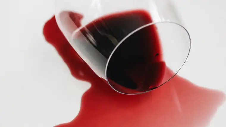 Tipped wine glass spilling a pool of red wine across a white surface