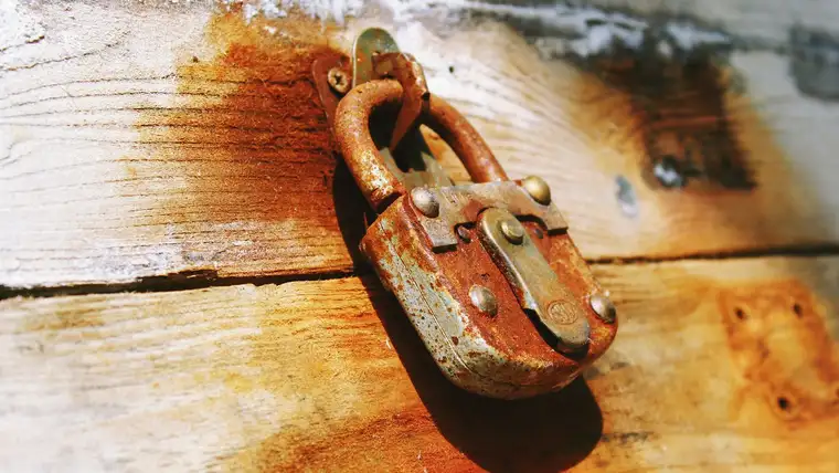 Rusty old padlock leaving orange rust stains running down weathered white wood
