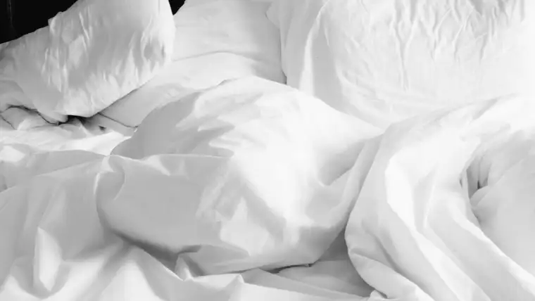 Rumpled white bed sheets and pillows on an unmade bed
