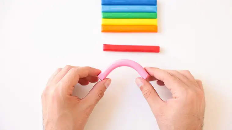 Hands bending a pink putty stick beside bars of colorful modeling clay
