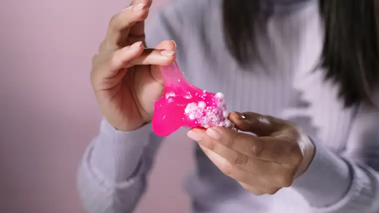 Hands stretching bright pink slime with white beads over a lavender sweater