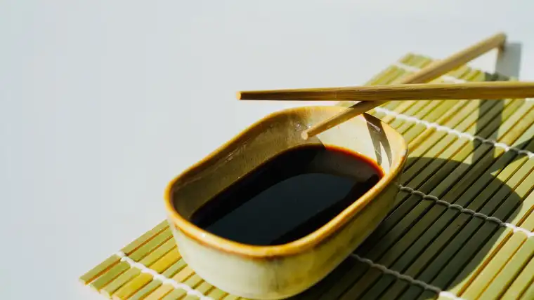 Ceramic dish of dark soy sauce with chopsticks on a bamboo mat