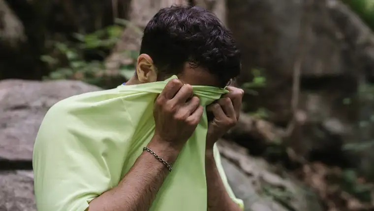 Man wiping his sweaty face with the front of a lime green T-shirt outdoors