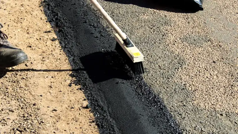 Broom spreading sticky black tar sealant along a strip of road surface