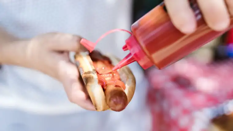 Ketchup squeezed onto a hot dog held over a white shirt