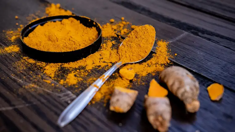 Bright yellow turmeric powder spilling from a bowl and spoon with fresh roots