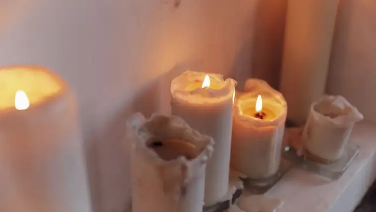 Burning pillar candles with melted wax dripping down onto a white shelf