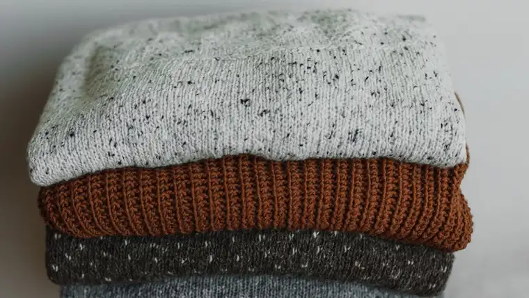 Stack of neatly folded knit sweaters in gray, rust and charcoal