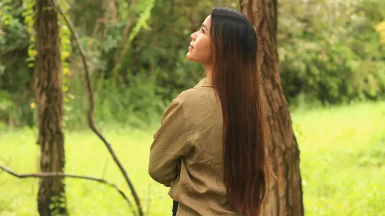 Woman seen from behind with long straight dark brown hair in a green park
