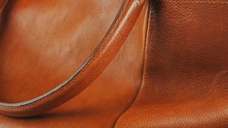 Close-up of a smooth tan leather bag with a stitched handle