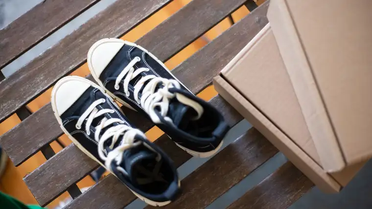 Pair of black canvas high-top sneakers on a wooden bench beside a shoebox