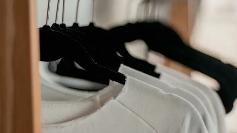Row of white T-shirts hanging on black velvet hangers in a closet